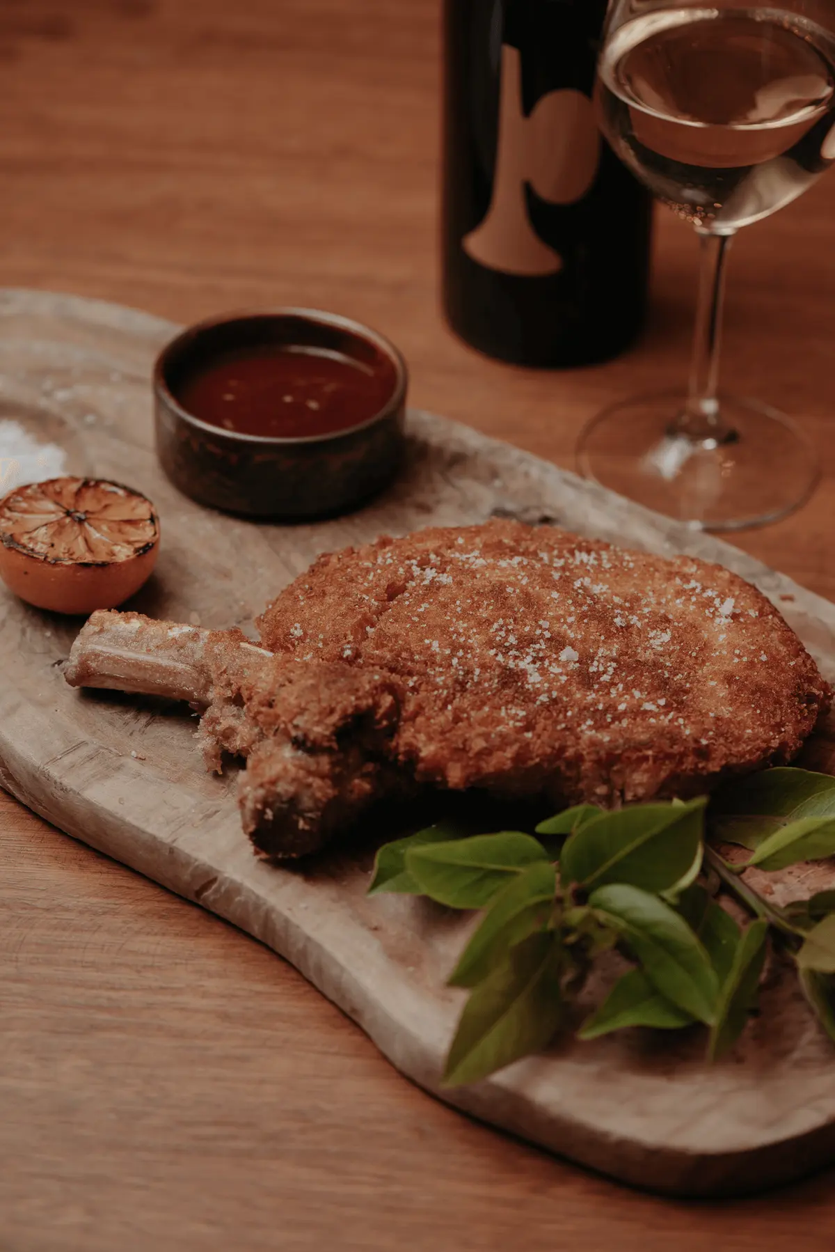A breaded cut served on a wooden board with grilled corn and broccolini