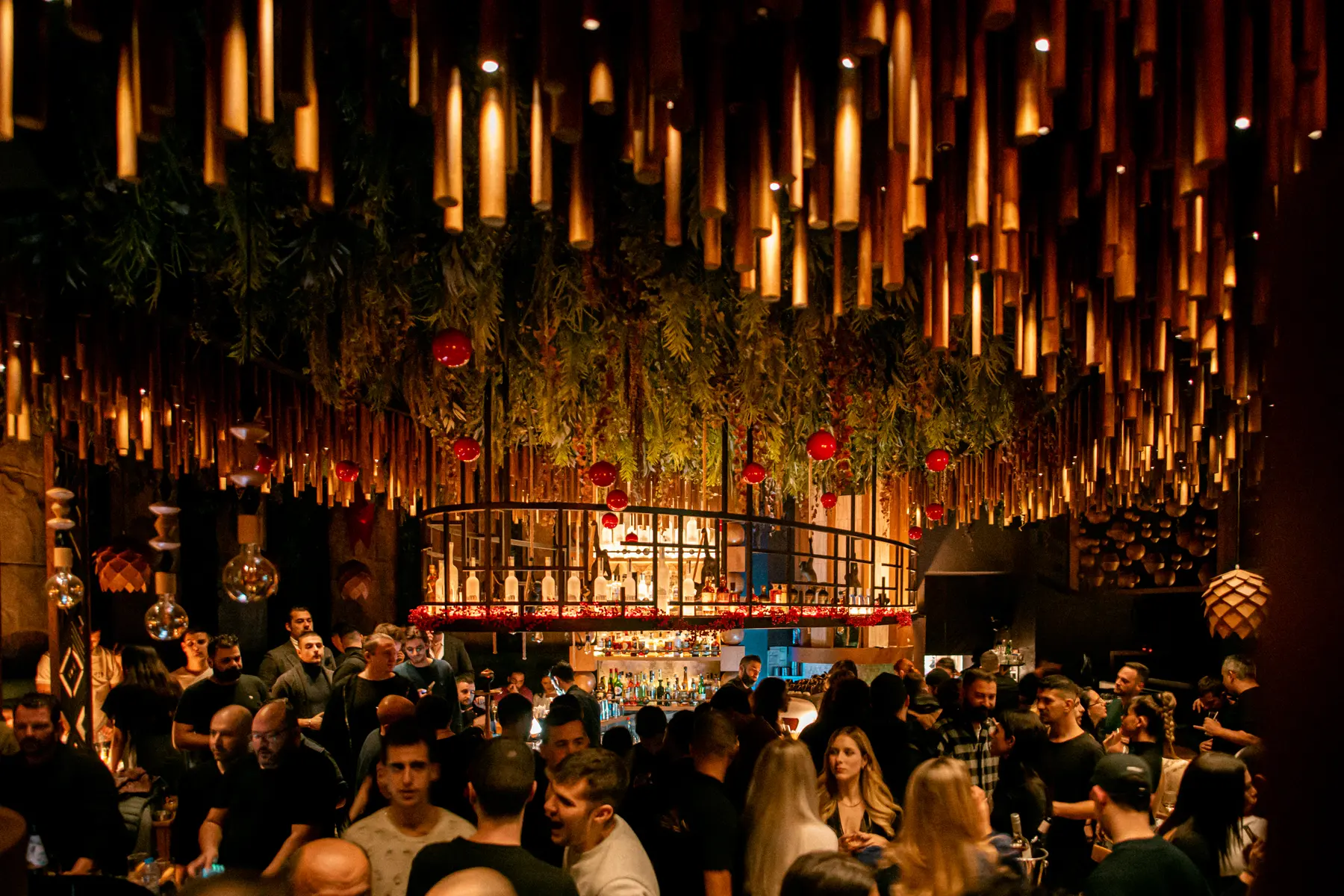 Guests crowding the bar under the bamboo lights at a private party at Iguazu Athens