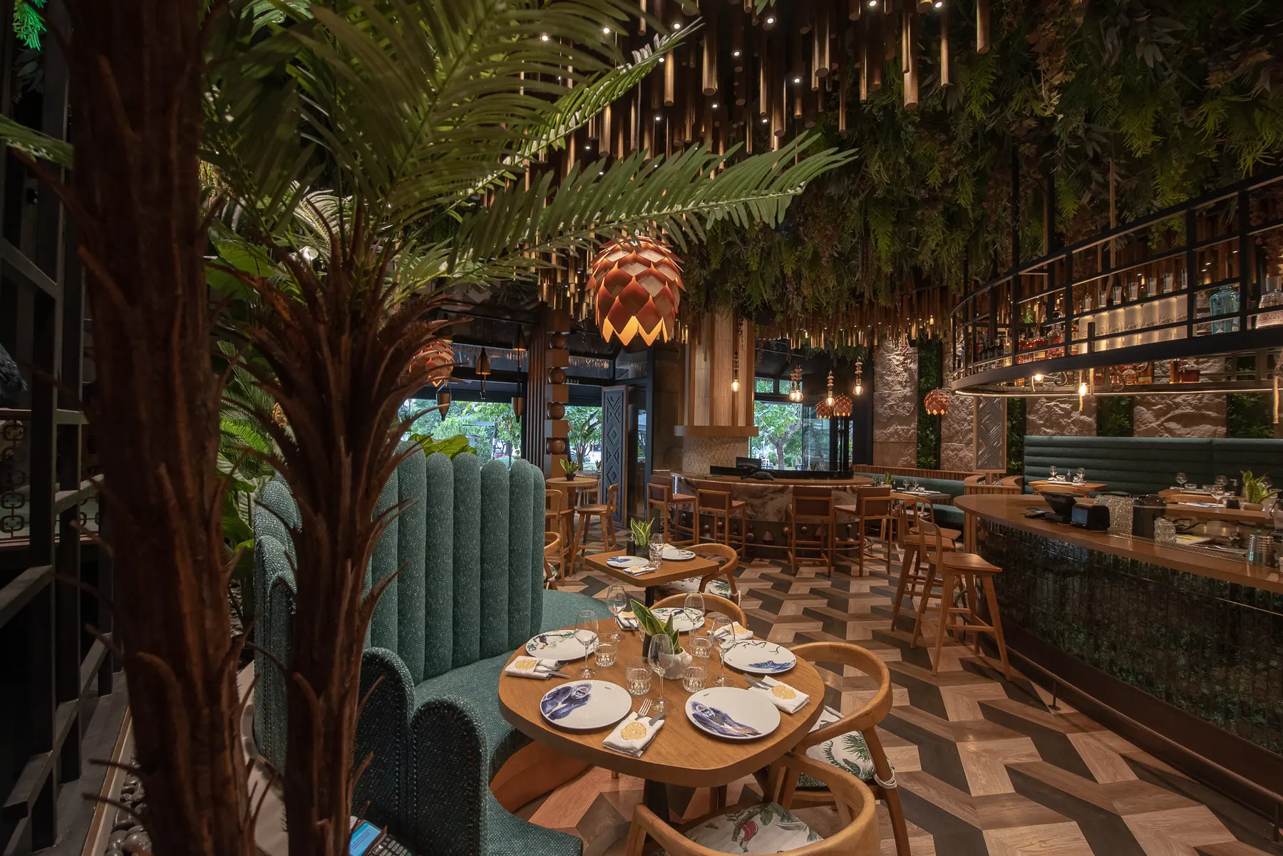 The dining room at Iguazu Athens, with a palm in the foreground, hanging bamboo across the ceiling and green velvet banquettes